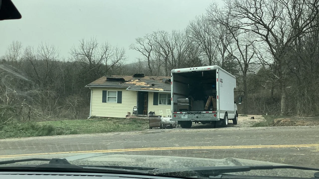 House with roof and siding damage after a tornado, seen with a truck